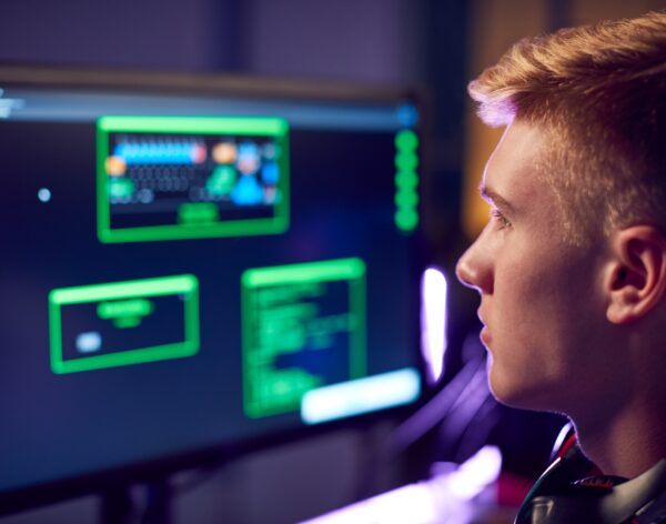 Male Teenage Hacker Sitting In Front Of Computer Screens Bypassing Cyber Security