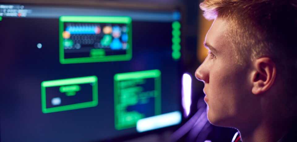Male Teenage Hacker Sitting In Front Of Computer Screens Bypassing Cyber Security