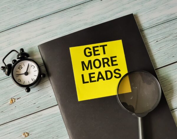 Phrase get more leads written on sticky note with alarm clock,magnifying glass and book.