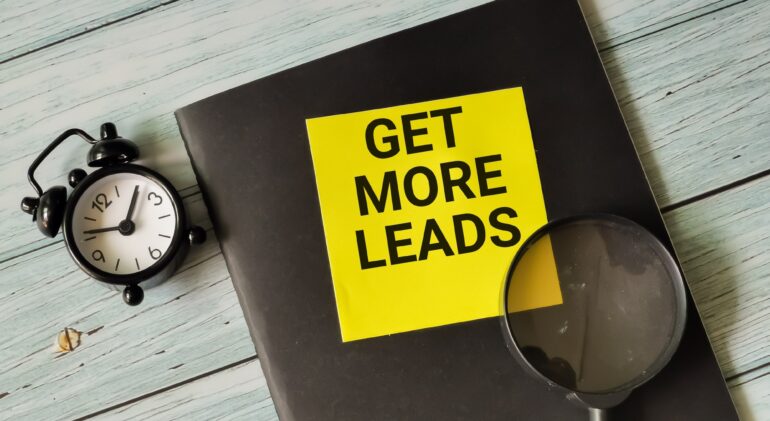 Phrase get more leads written on sticky note with alarm clock,magnifying glass and book.